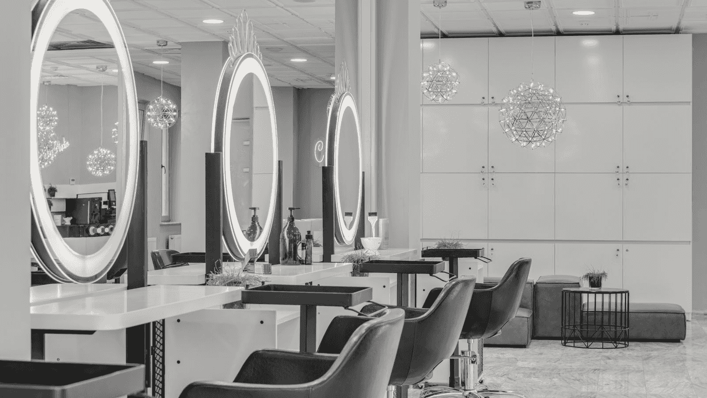 Round lit mirrors in a row over salon chairs.