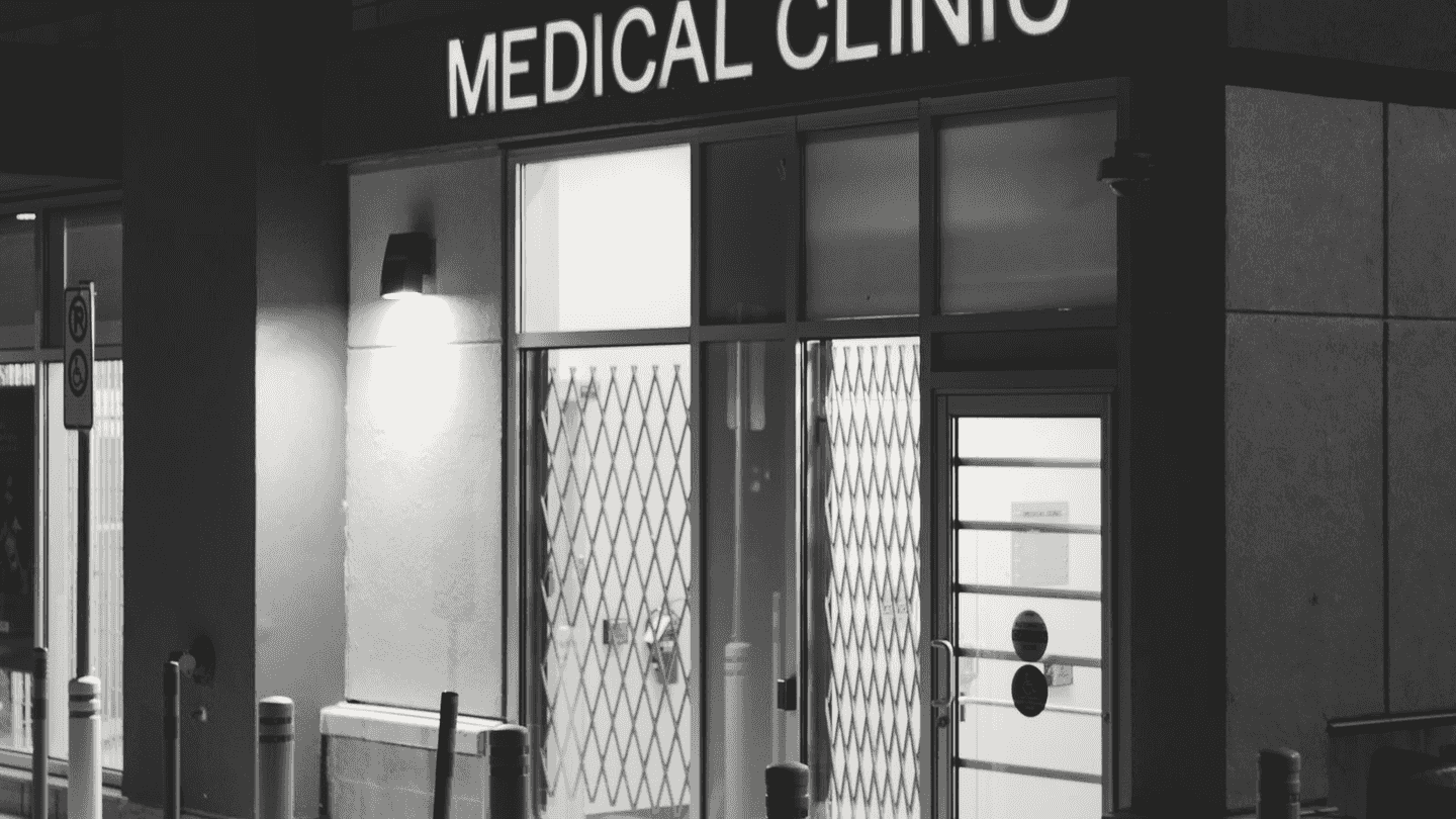 A clinic front at night, its sign lit over the door.