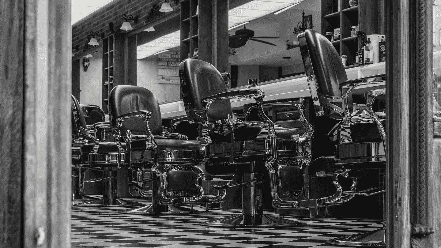 A row of old barber chairs on a checkerboard floor.