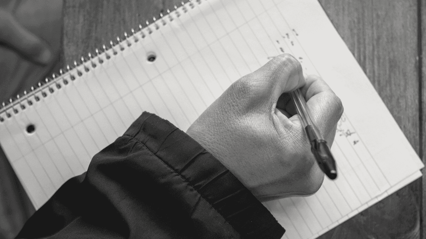 A hand writing on a notepad on a counter.