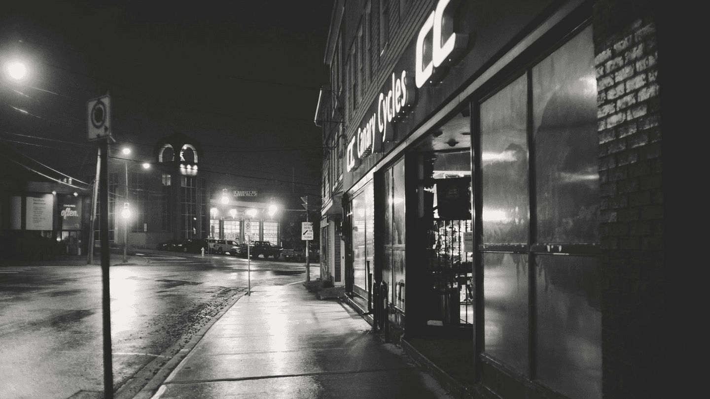 An empty street at night, one shop lit further down.
